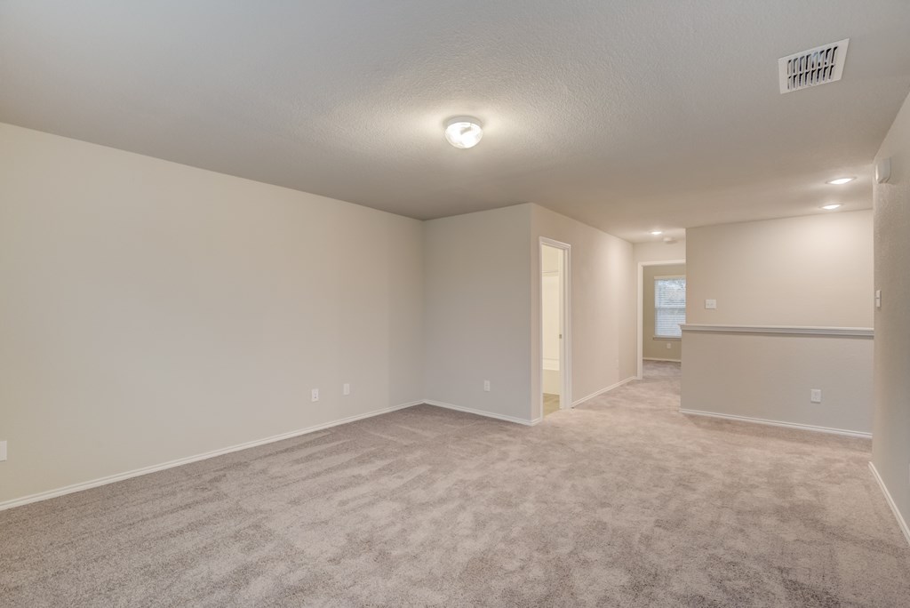 an empty living room with carpet and a door to a kitchen