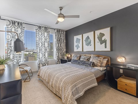 Luxury Apartments Near Pearl Theater - Flatiron LV - Spacious Bedroom With Plush Carpeting, Ceiling Fan, Large Windows, Patterned Curtains, And Modern Furnishings