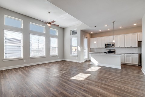 Houston, TX, Rental Homes - East Heights - Unfurnished Living Room with Vinyl Plank Flooring, Ceiling Fan, Large Windows, and View of Kitchen.