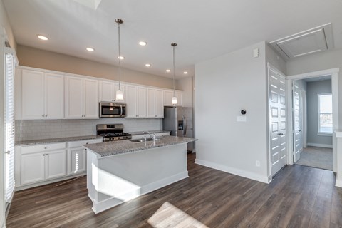 Rental Homes in Houston, TX - East Heights - Kitchen with Vinyl Plank Flooring, White Cabinetry, Stainless Steel Appliances, Granite Countertops, Kitchen Island with Pendant Lights, and Tile Backsplash.