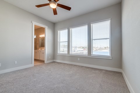 Luxury Three-Bedroom Homes for Rent in Houston, TX - East Heights - Carpeted Bedroom with Large Windows, Soft Grey Walls, Attached Bathroom, and Ceiling Fan.