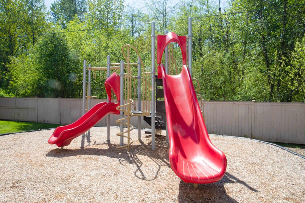 Puyallup WA Apartments - One Canyon Place - Fenced-In Playground with 2-Slide Tower Set and Lush Trees