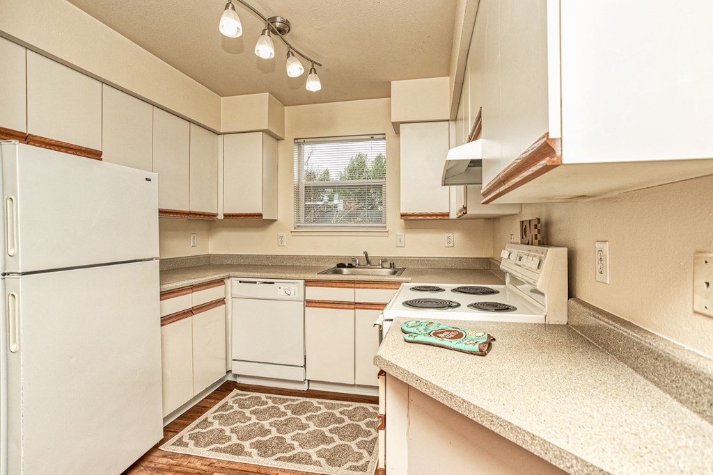 Dog-Friendly Garden-Style Apartments in University Place, WA - Carriage House - Kitchen with Wood-Style Flooring, Custom Cabinetry, Light Fixtures, 4-Burner Range, Range Hood, Refrigerator, and Dishwasher.