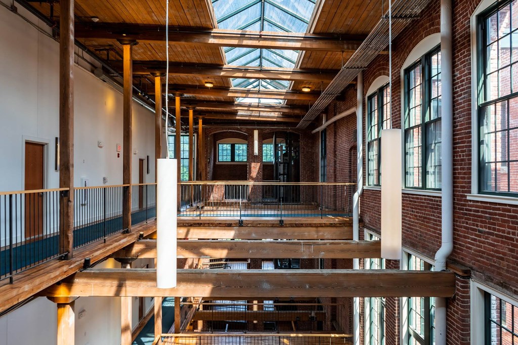 Interior view of a renovated mill building with exposed brick, wooden beams, skylights, and multi-level walkways.