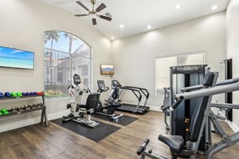 A well-equipped home gym with a variety of exercise machines and a flat-screen TV mounted on the wall.