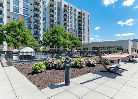A modern outdoor seating area with a table and chairs is surrounded by a garden with flowers and trees.
