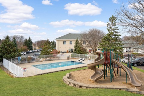 A playground with a slide and a pool in the background.