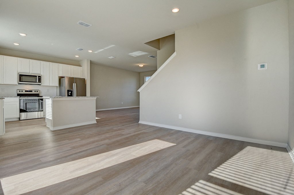 an empty living room and kitchen with white cabinets and wood flooring