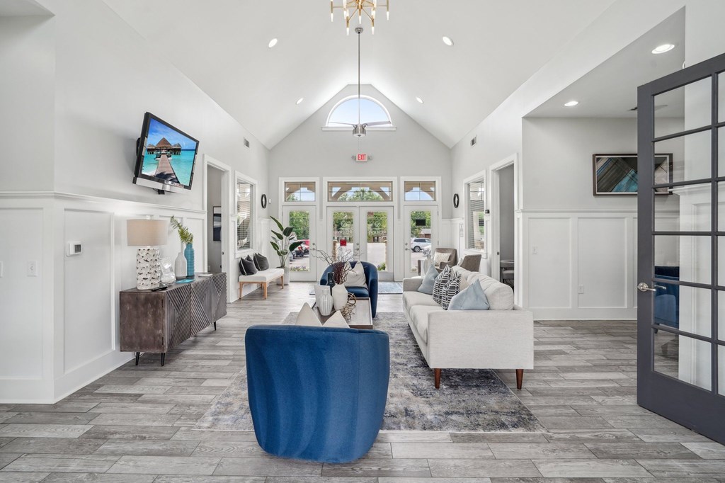 Bright, modern apartment clubhouse lounge area with white walls, vaulted ceiling, and blue accent furniture.