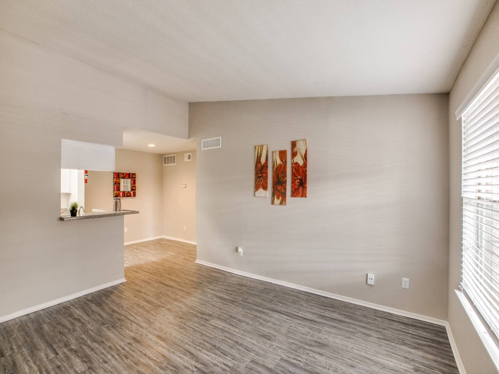 the living room and kitchen of an apartment with wood flooring and a window