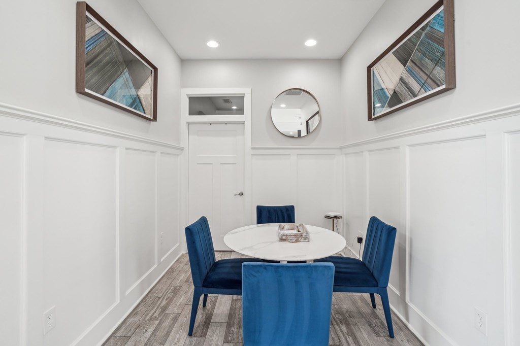 Dining nook with white walls, blue velvet chairs, and a marble-topped table.