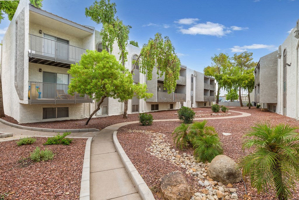 One Bedroom Apartments in Phoenix, AZ - Adrella on 28th - Walkway with Green Trees and Landscaping Rocks.