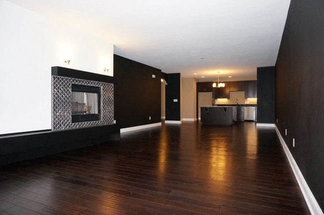 an empty living room with a fireplace and a kitchen in the background