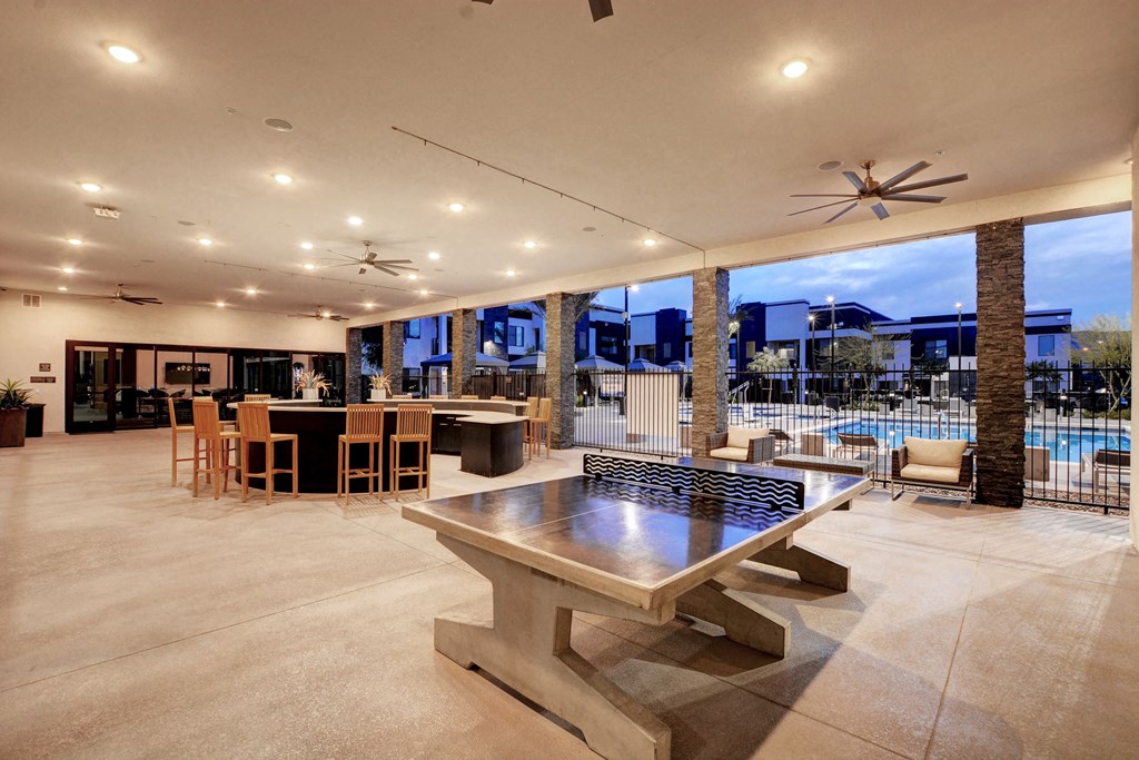 a large patio with a ping pong table and a pool in the background and cocktail bar