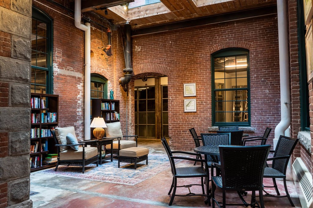 Brick-walled library lounge with bookshelves, armchairs, and tables under a skylight.