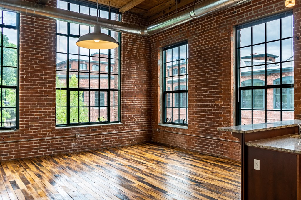 Loft apartment interior with exposed brick walls, hardwood floors, and large windows.