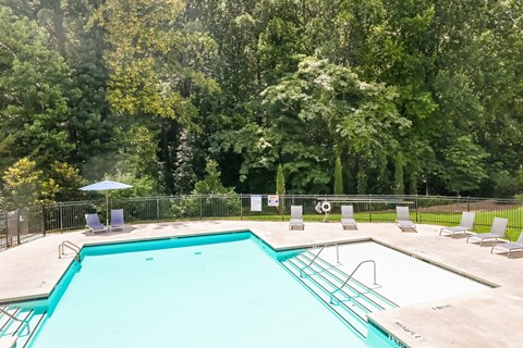 A large swimming pool surrounded by trees and chairs.