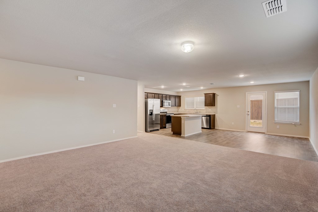 the living room and kitchen of an apartment with a carpeted floor and white walls