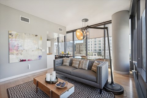 A modern living room with a grey couch and a large painting on the wall.