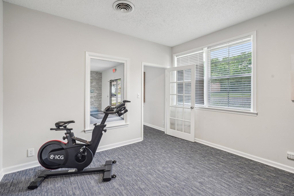 Indoor cycling bike in a bright, carpeted fitness room with natural light.