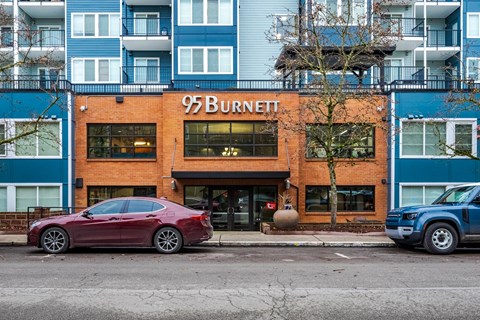 A red car is parked in front of a building with the sign 95 Burnett.