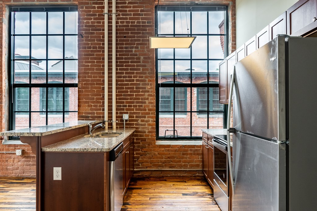 Kitchen in a loft apartment with exposed brick walls, stainless steel appliances, and large windows.