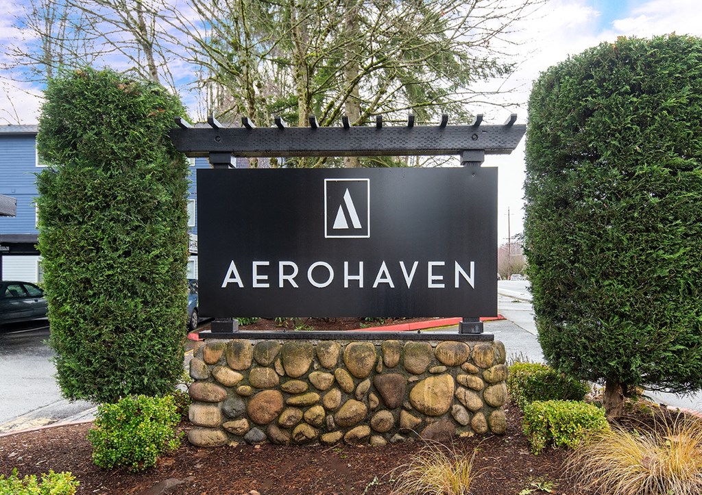 a sign in front of a driveway with a stone wall and bushes