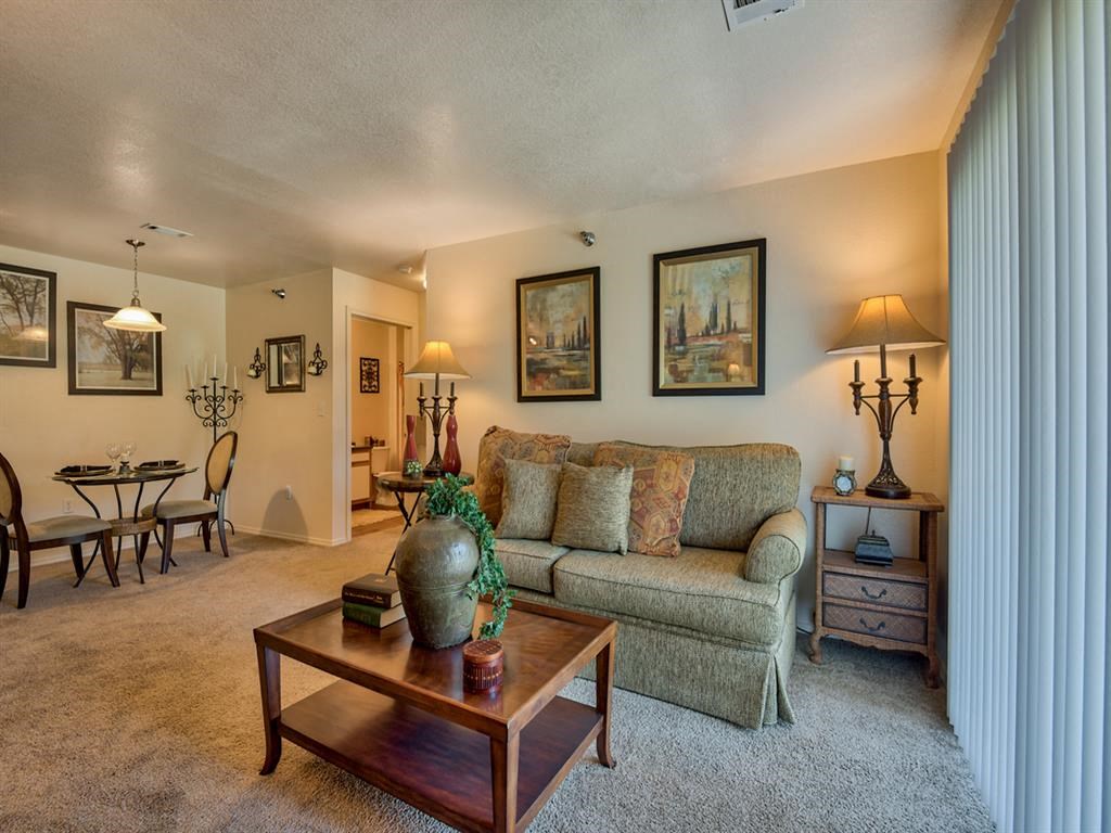 Living room with carpet, windows with blinds, couch, dinner table with chairs, coffee table and wall decor