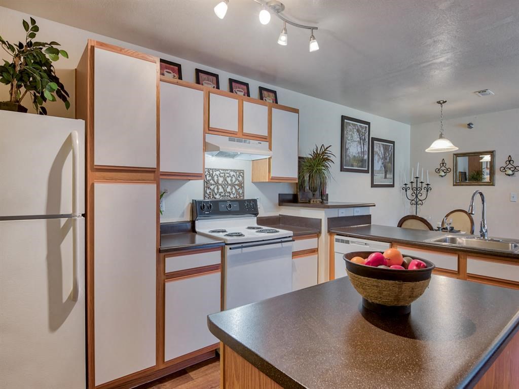Kitchen with stainless steel sink, black countertop island, stove top with oven, plenty of cabinetry, wood floors and living room in back