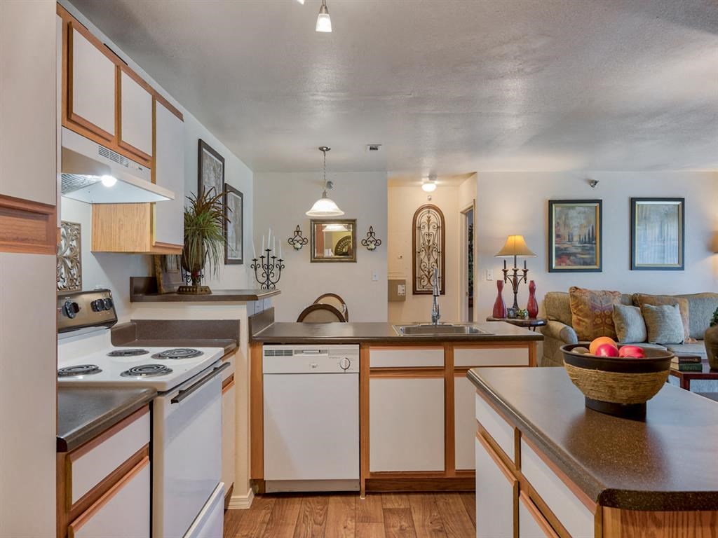 Kitchen with stainless steel sink, black countertop island, stove top with oven, plenty of cabinetry, wood floors and living room in back