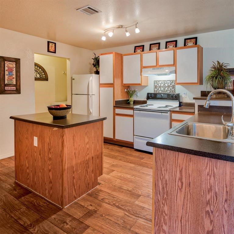 Kitchen with stainless steel sink, black countertop island, stove top with oven, plenty of cabinetry, and wood floors