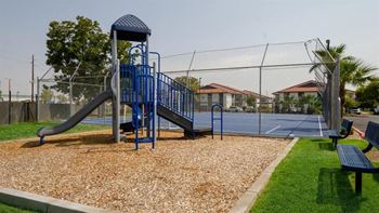 a playground with a slide and monkey bars in front of a tennis court