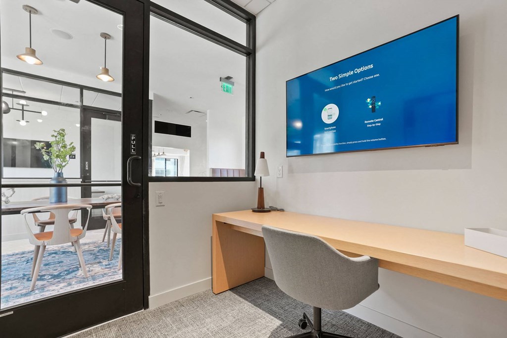 a desk in an office with a large screen on the wall