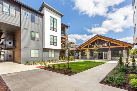 A modern building with a grey and brown exterior and a landscaped front yard.