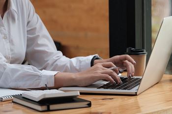A person in a white shirt is typing on a laptop.
