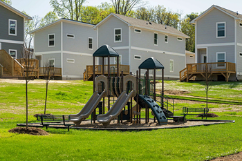 A playground with a green canopy and a slide in the middle of a grassy area.