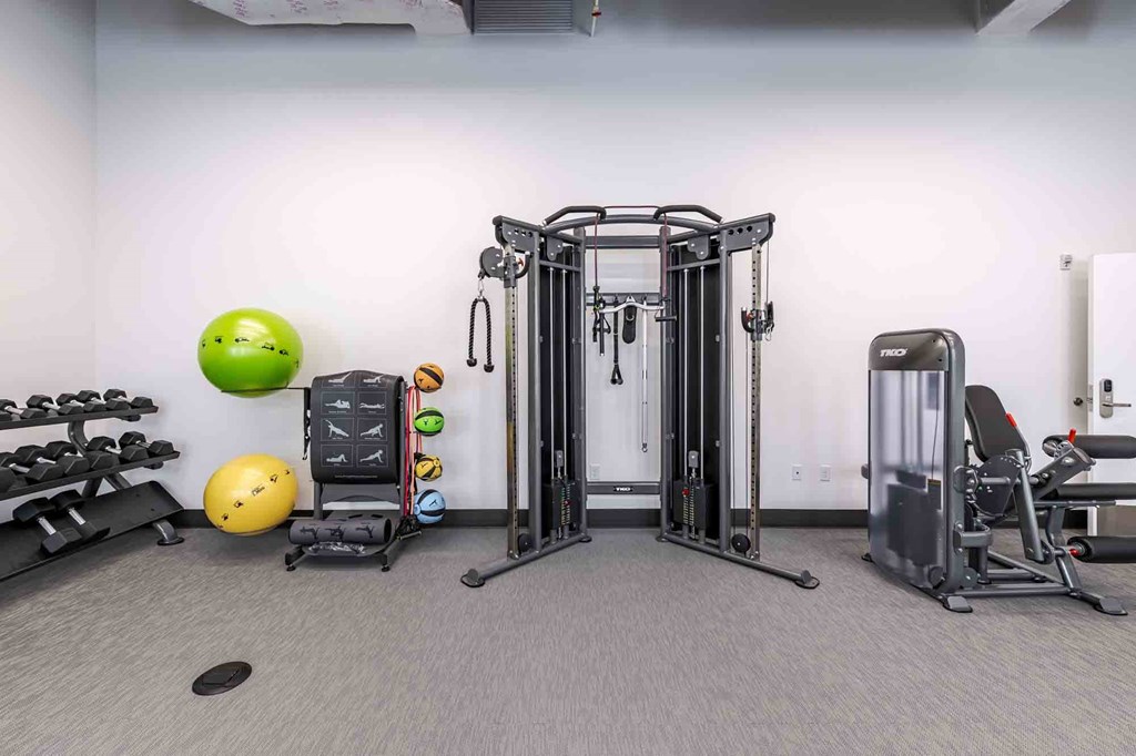 A gym with a variety of equipment including a leg press machine, a weight bench, and a dumbbell rack.