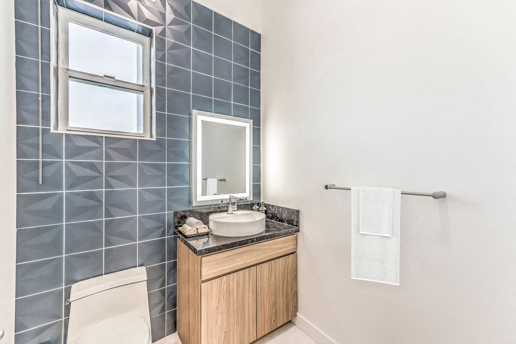 a bathroom with grey tiles and a wooden cabinet with a sink and toilet