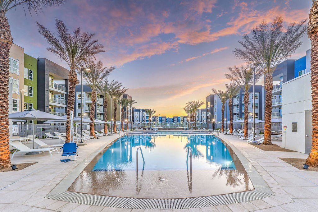 an outdoor pool with palm trees and buildings in the background