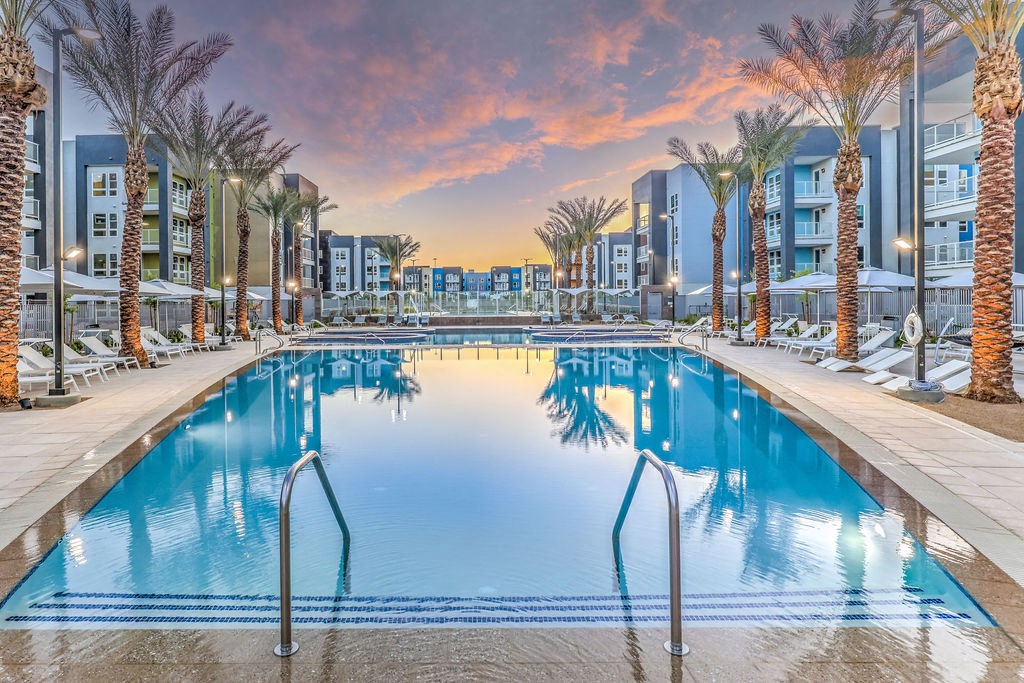 a large swimming pool with palm trees and buildings in the background