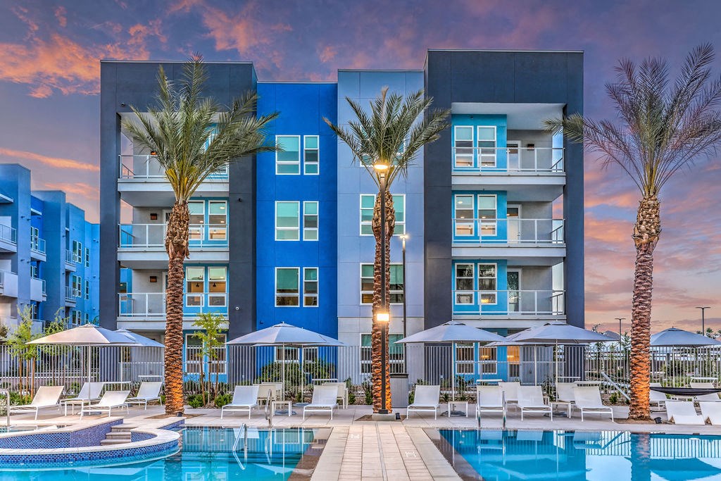 an outdoor pool with lounge chairs and umbrellas in front of an apartment building