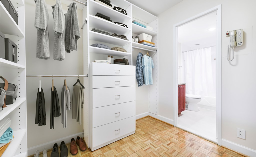 A white closet with clothes hanging and shoes on the floor.