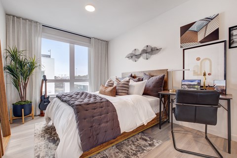 a bedroom with a bed and a desk and a large window