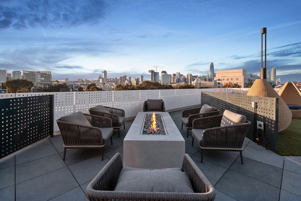 a rooftop patio with chairs and a fire pit and a city in the background