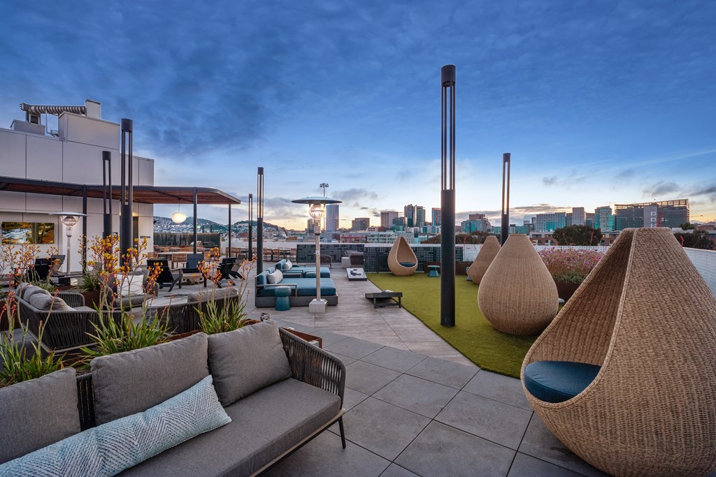 a rooftop patio with couches and chairs and a city in the background