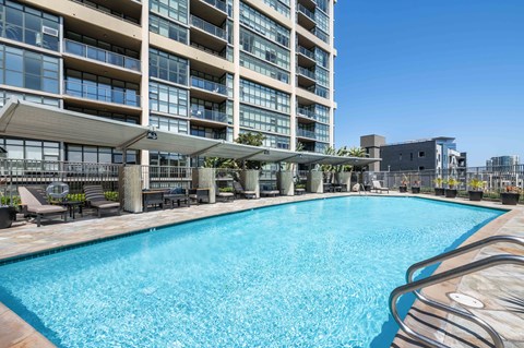 Apartments in Irvine, CA, for Rent - Astoria at Central Park West - Resort-Style Outdoor Pool With Clear Blue Water, Sun Loungers, Pergola Seating, and High-Rise Apartment Building Views.