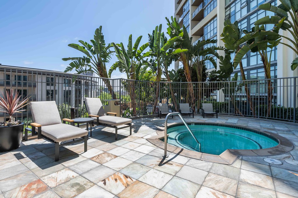 Pet-Friendly Apartments in Irvine, CA - Astoria at Central Park West - Spa with Lounge Seating, Surrounded by Grey Fencing, Potted Plants, and Tropical Trees.
