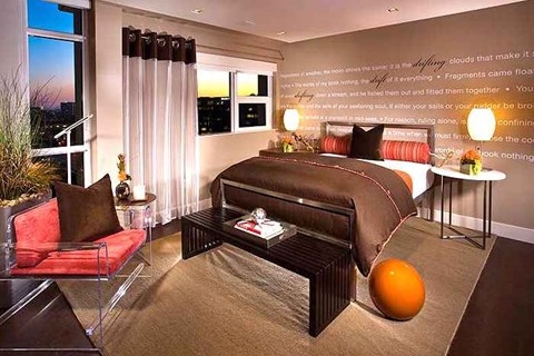 Dog-Friendly Apartments in Irvine, CA - Astoria at Central Park West - Modern Bedroom With Plush Bed, Typography Accent Wall, Side Lamps, Armchair, Bed Bench, and Large Corner Windows.