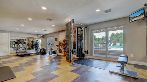 Two-Bedroom Apartments in Aurora, CO - Aurora Hills - Fitness Center With Treadmill, Elliptical, Stationary Bike, Cable Machine, Weight Bench, Large Mirrors, Mounted Monitors, and Poolside Windows.