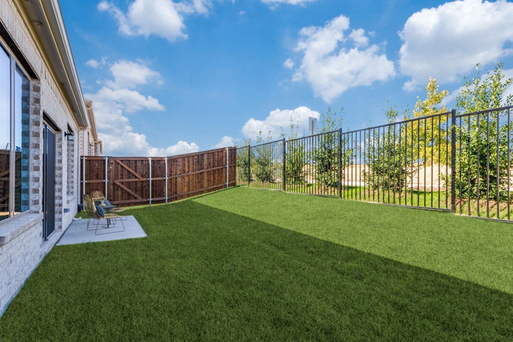 A backyard with a green lawn and a black fence.
